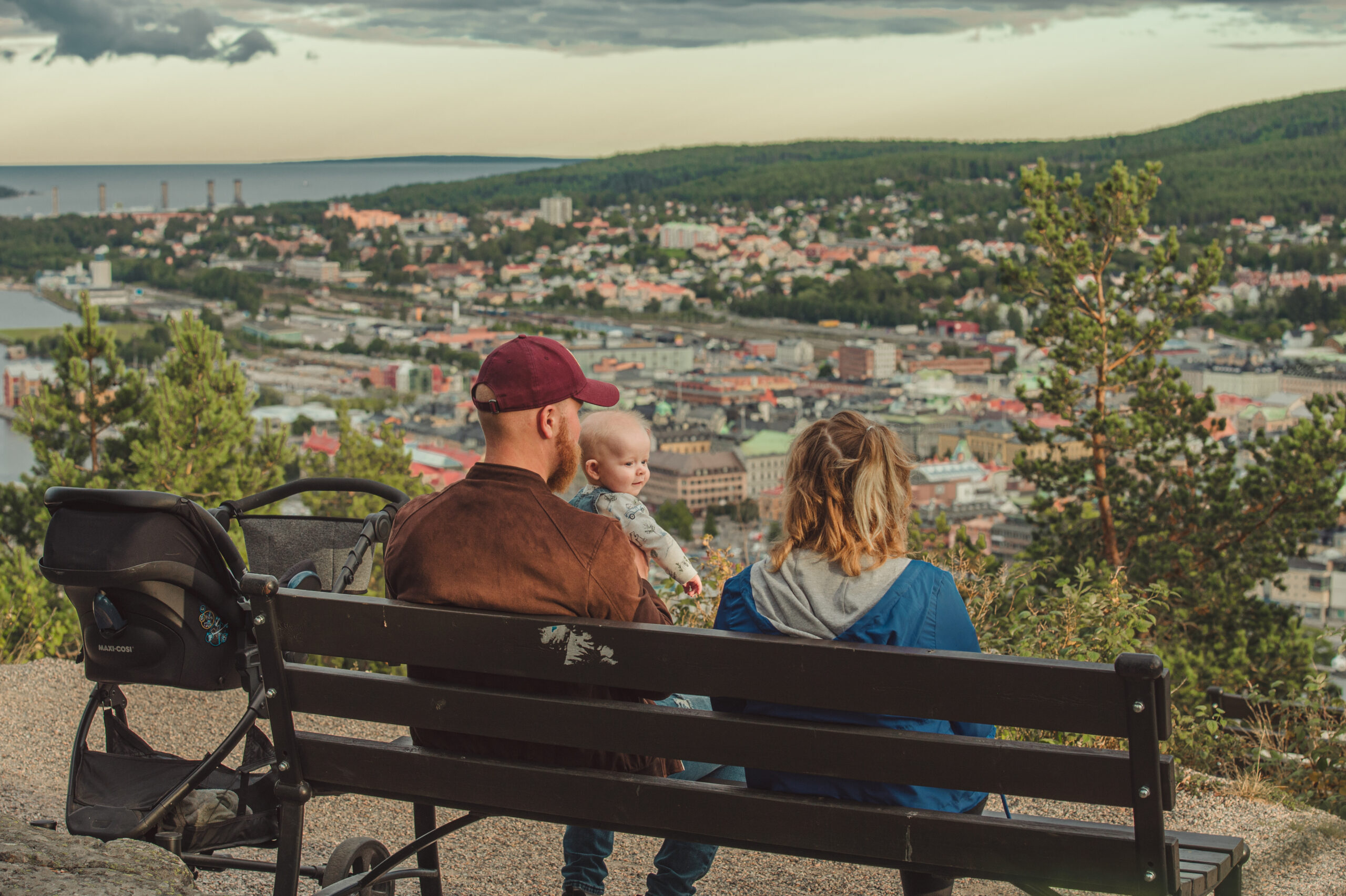 Ett par sitter på en bänk med en bebis i famnen och blickar ut över Sundsvall.
